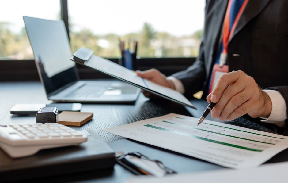 Imagem de um profissional de negócios analisando relatórios e utilizando dispositivos eletrônicos em uma mesa de escritório moderna, com foco em produtividade e estratégia corporativa.