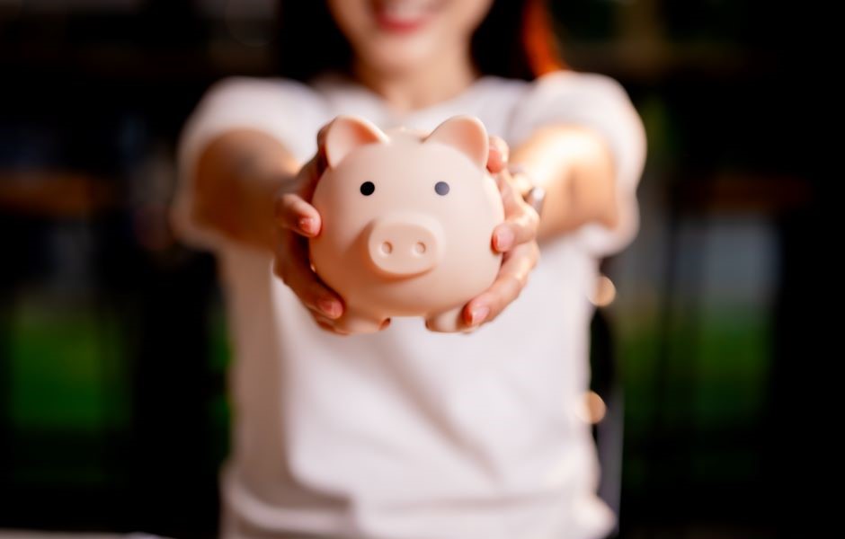 Pessoa segurando um cofrinho de porquinho rosa, simbolizando poupança e economia, em um ambiente ao ar livre. Imagem que incentiva a economia financeira e a educação financeira.