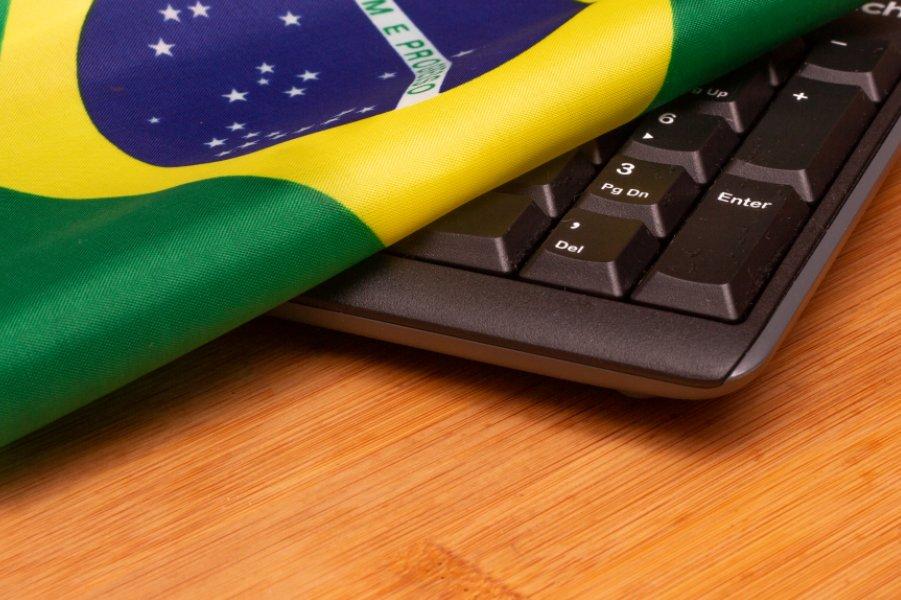 Bandeira do Brasil sobreposta a um teclado de computador preto em cima de uma mesa de madeira.