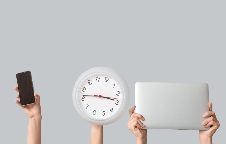 Três mãos segurando diferentes objetos: uma com um celular, outra com um relógio e a última com um laptop, contra um fundo cinza claro.
