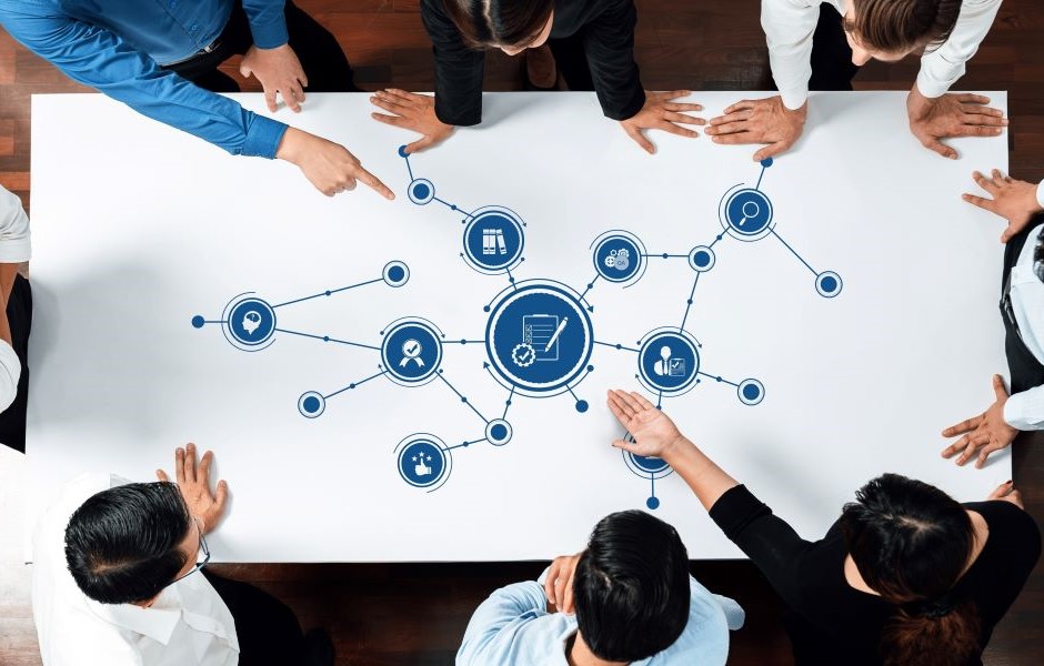 Reunião de equipe discutindo estratégias de negócios em volta de uma mesa com gráfico e ícones de comunicação, inovação e tecnologia.